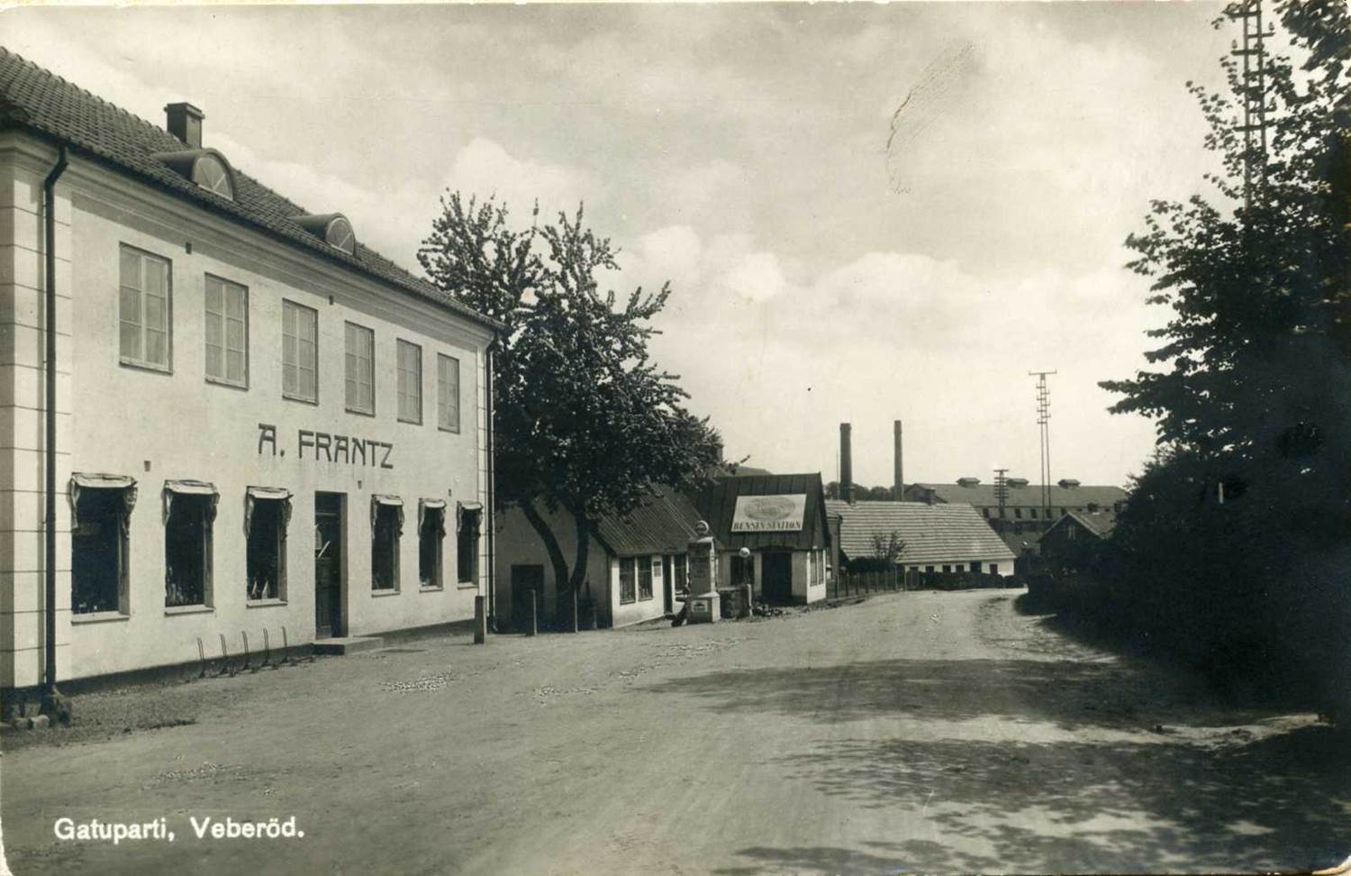Gatuparti i Veberöd på ett historiskt vykort, med butiken A. Frantz och en bensinstation längs grusvägen