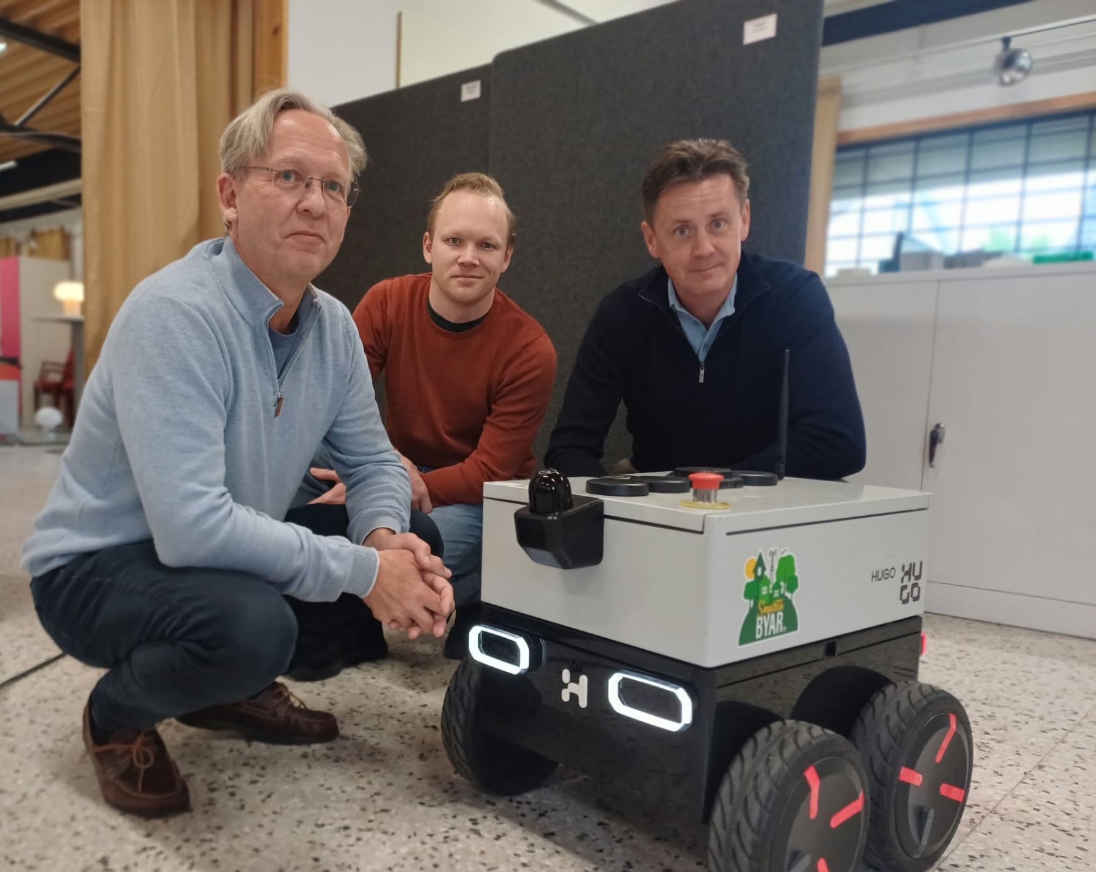 Tre personer tillsammans med Hugo-roboten i en verkstad